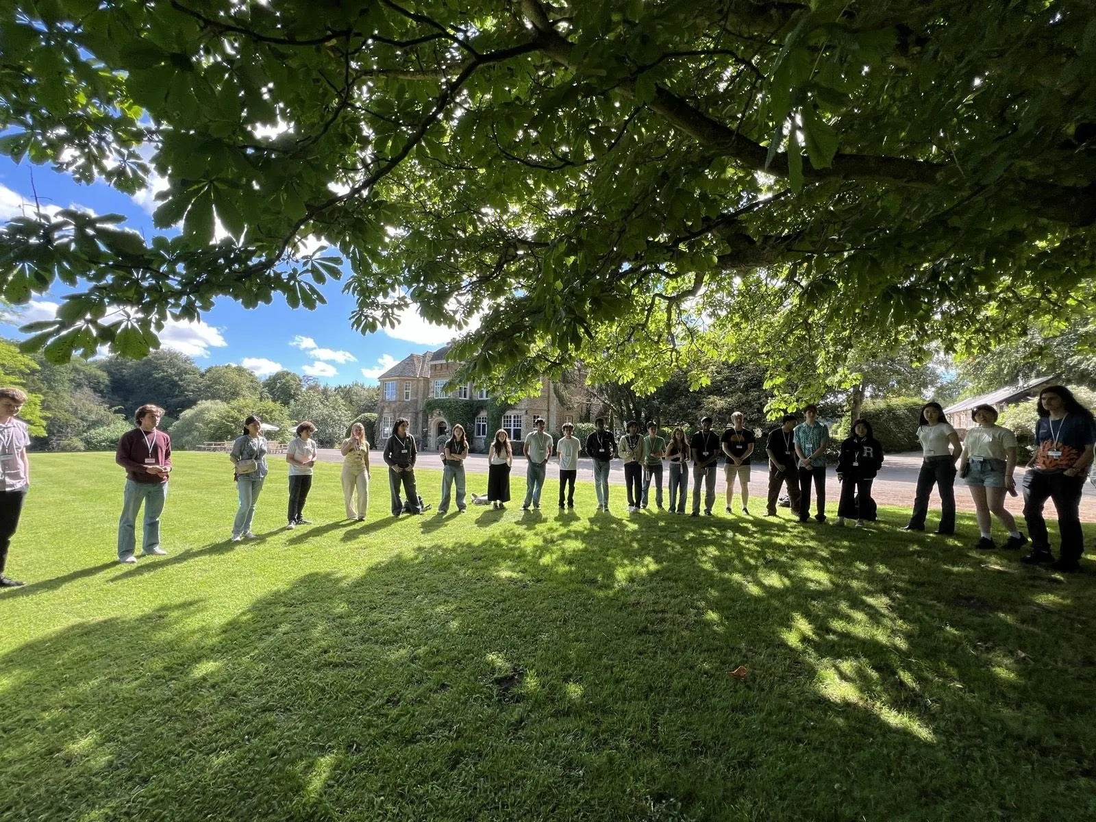 Attendees standing in a wide circle on a lawn under a tree