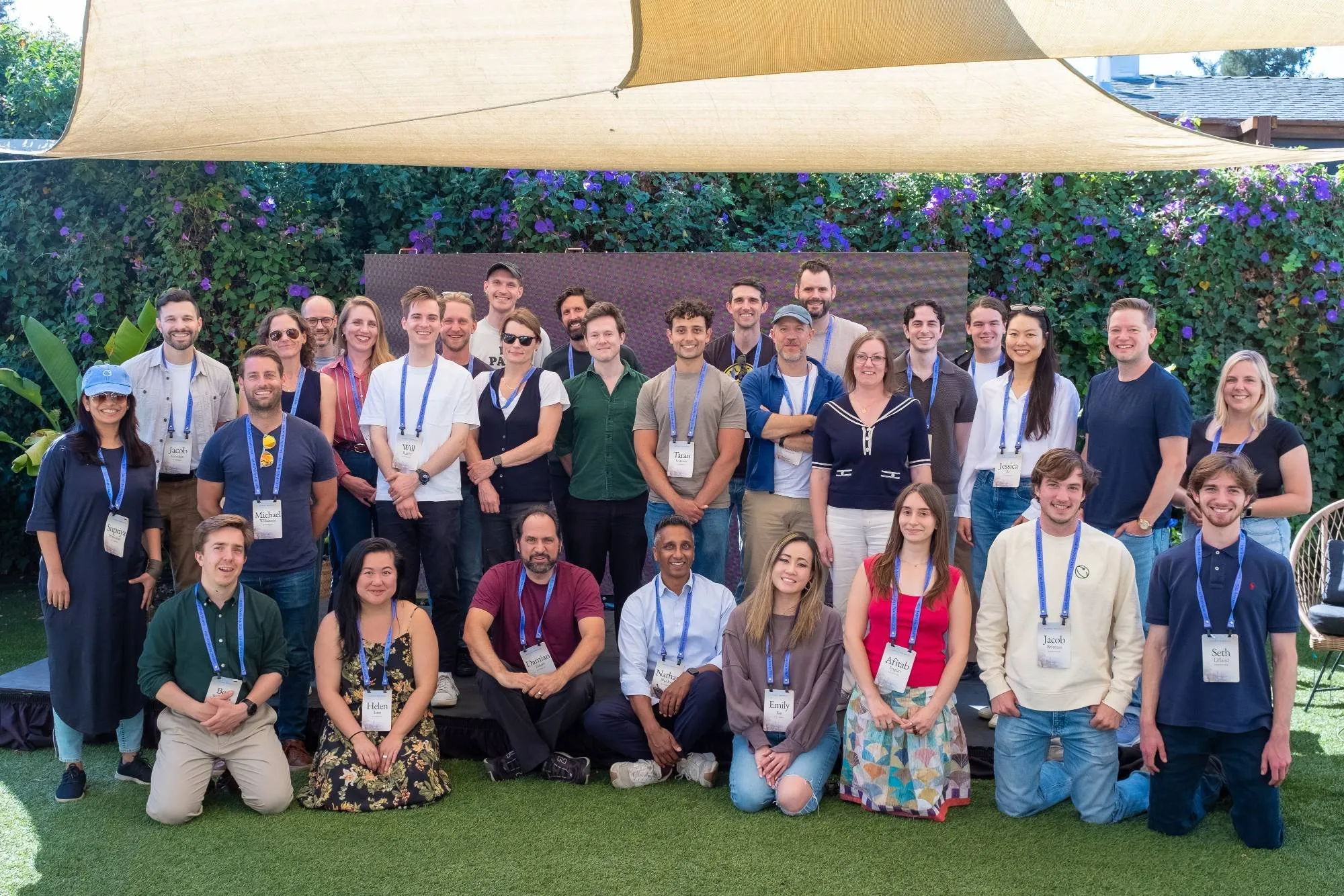 A workshop cohort posing together on a lawn under a shade sail